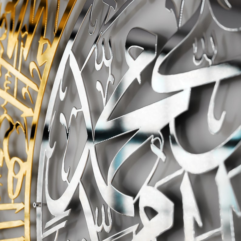 May include: A silver metal wall decor with intricate Arabic calligraphy. The design is cut out of the metal, creating a three-dimensional effect.