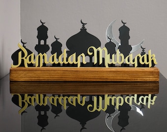 May include: A wooden sign with a gold inscription of "Ramadan Mubarak" and black silhouette cutouts of mosques and a crescent moon.
