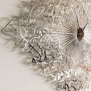 May include: A silver-colored wall clock with a unique design featuring Arabic calligraphy. The clock has a radial pattern with thin lines emanating from the center, where the clock hands are located. The hands are black with a red second hand.