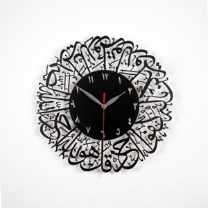 K&ouml;nnte beinhalten: Schwarze Wanduhr mit arabischer Kalligraphie um das Zifferblatt. Das Zifferblatt hat schwarze Zeiger und wei&szlig;e Zahlen.