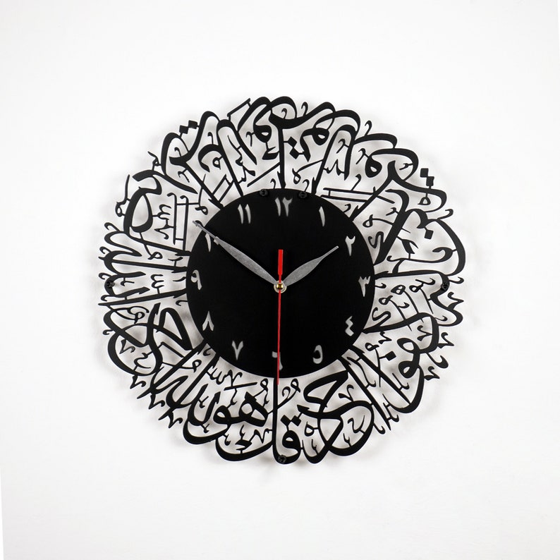 K&ouml;nnte beinhalten: Schwarze Wanduhr mit arabischer Kalligraphie um das Zifferblatt. Das Zifferblatt hat schwarze Zeiger und wei&szlig;e Zahlen.