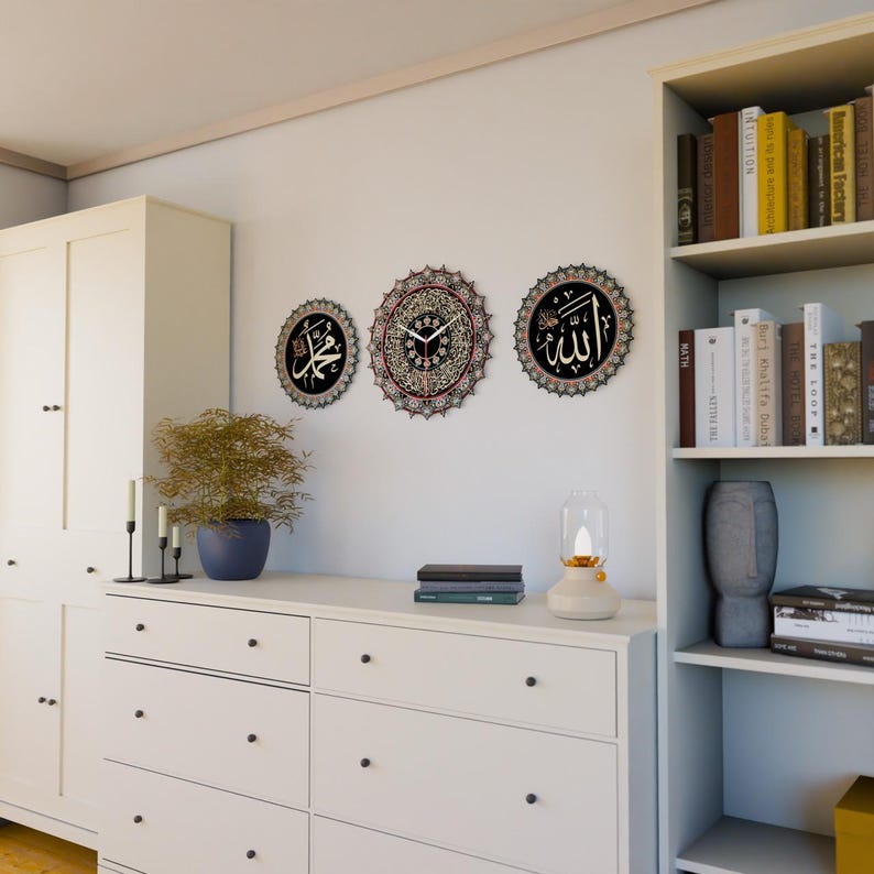 Op de afbeelding: Drie decoratieve wandklokken met zwarte en gouden Arabische kalligrafie op een witte achtergrond. De klokken zijn rond en hebben ingewikkelde ontwerpen. De middelste klok heeft een witte wijzerplaat met zwarte wijzers.
