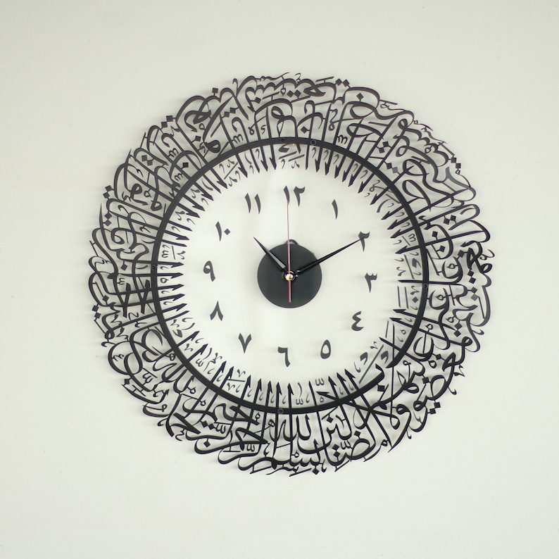 May include: A black and white clock with Arabic calligraphy around the face. The clock face has black Roman numerals and black hands.