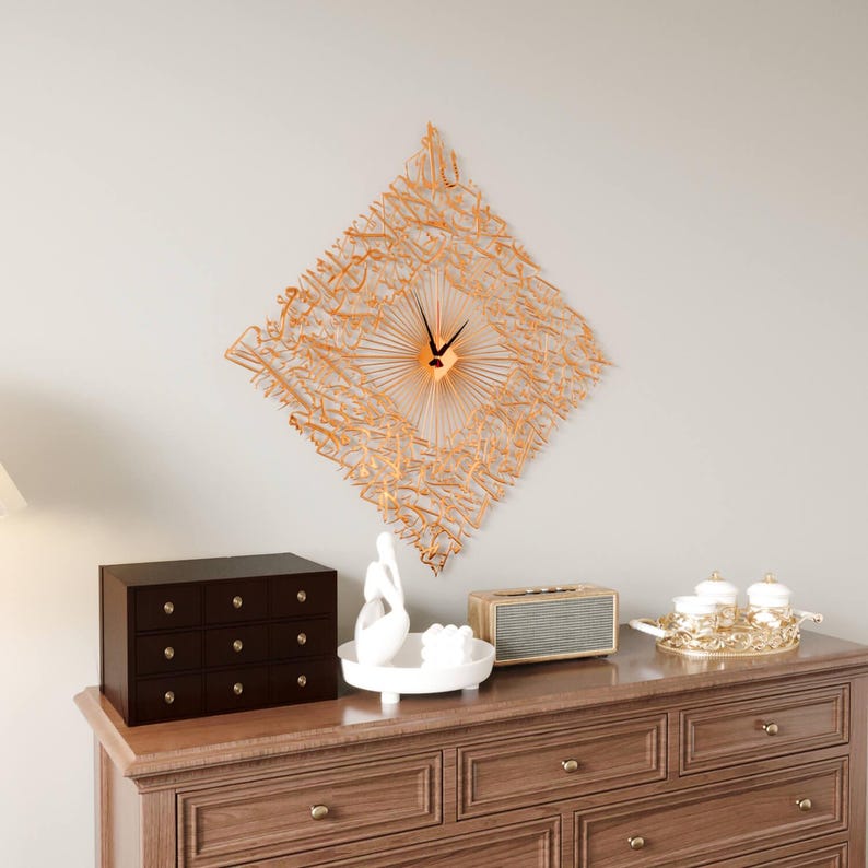 May include: A decorative wall clock with a diamond-shaped, openwork design in a warm, golden hue. The clock features black hands and a central sunburst pattern. The clock is mounted on a light gray wall above a wooden dresser.