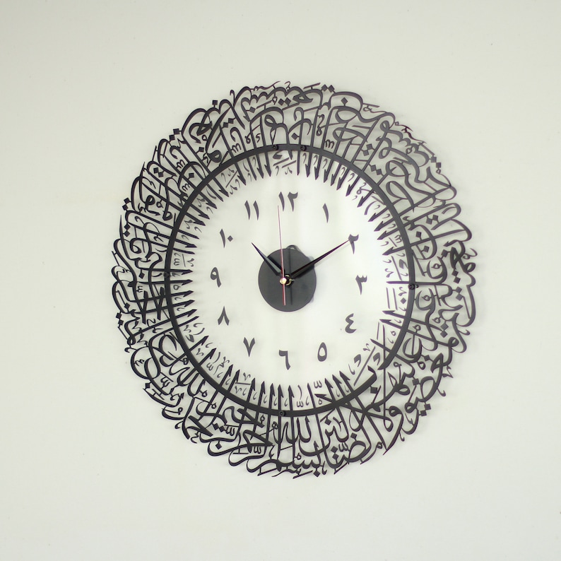 May include: A black and white clock with Arabic calligraphy around the edge. The clock face has black Roman numerals and black hands.
