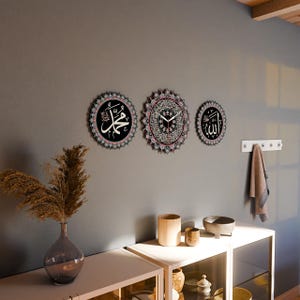 Op de afbeelding: Drie ronde wandklokken met ingewikkelde zwart-witte ontwerpen. De klokken bevatten Arabische kalligrafie, waaronder de woorden "Allah" en "Muhammad".