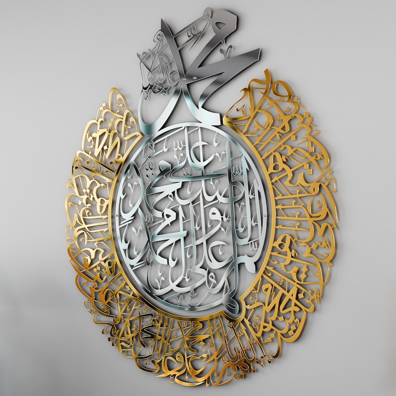 May include: A silver and gold metal wall art featuring intricate Arabic calligraphy. The design is circular with a central silver section and a gold outer ring. The calligraphy is in a traditional style and is likely a religious inscription.