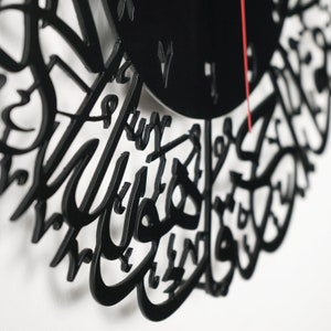 K&ouml;nnte beinhalten: Schwarze Uhr mit arabischer Kalligrafie. Das Zifferblatt ist schwarz mit wei&szlig;en Zahlen und einem roten Sekundenzeiger.
