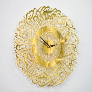 May include: Gold-colored wall clock with Arabic calligraphy surrounding the clock face. The clock face has black hands and Roman numerals.