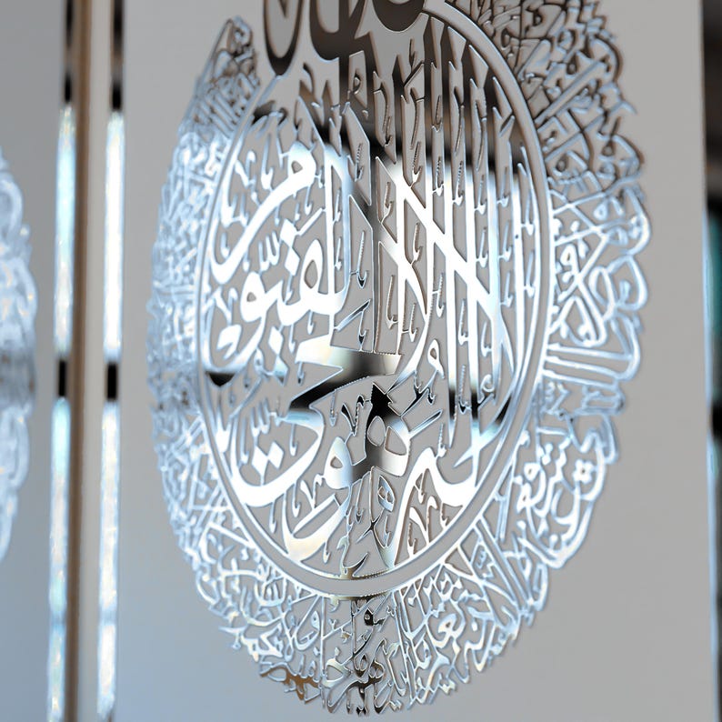 May include: A silver metal wall hanging with intricate Arabic calligraphy in a circular design.