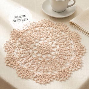 Puede incluir: Un tapete de ganchillo de color melocotón suave, con un intrincado diseño calado. El tapete es circular y descansa sobre una superficie blanca, con una taza y un platillo visibles en el fondo. El texto "PDF PATTERN NO PHYSICAL ITEM" está en la esquina superior izquierda.