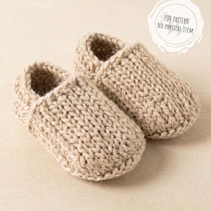 May include: A pair of beige knitted slippers. The slippers are made of a thick yarn and have a textured appearance. The image includes the text "PDF PATTERN NO PHYSICAL ITEM".