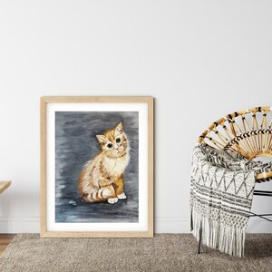 May include: A framed watercolor painting of a ginger kitten sitting on a gray background. The kitten has white markings on its face and chest. The frame is made of wood and has a light brown finish.
