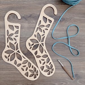 Può includere: Due appendini per calzini in legno con un design floreale. Gli appendini sono in legno marrone chiaro e hanno un design ritagliato di fiori e foglie.