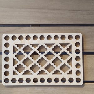 May include: A rectangular wooden decorative piece with a geometric quatrefoil pattern in the center and evenly spaced circular holes around the perimeter. The wood has a natural, light color.