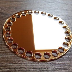 Könnte beinhalten: Ein runder, goldfarbener Acrylspiegel mit einem dekorativen Rand aus kleinen, runden Ausschnitten.