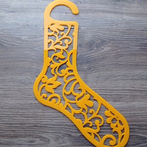 Può includere: Un portacalze di plastica giallo a forma di calza con un motivo floreale decorativo. Il portacalze ha un gancio in alto per appenderlo.