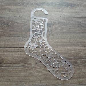 Könnte beinhalten: Eine transparente Socken-Schablone aus Kunststoff mit einem dekorativen Blumenmuster. Die Schablone ist zum Basteln und Dekorieren gedacht.