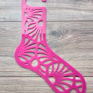 Può includere: Un portascarpe in plastica rosa con un design decorativo. Il portascarpe ha un gancio in alto per appenderlo.