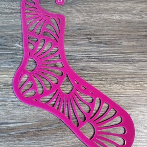 Può includere: Forma per calze in plastica rosa con un design di taglio decorativo. La forma ha un gancio in alto etichettato "S".
