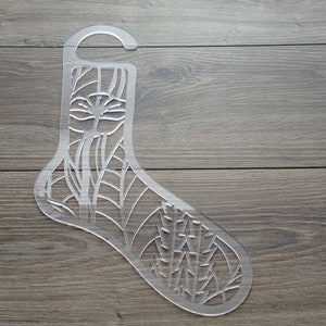 Può includere: Un appendiabiti per calzini in plastica trasparente con un design floreale. L'appendiabiti ha un gancio nella parte superiore per appenderlo.