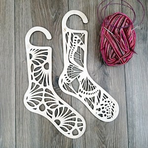 May include: Two wooden sock blockers with a decorative butterfly design. The blockers are shaped like a sock and have a hole at the top for hanging.