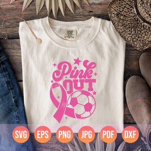 May include: A white t-shirt with a pink graphic design that says "Pink Out" with a pink ribbon and a soccer ball. The design is perfect for a sports team or a breast cancer awareness event.