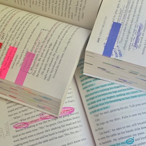 May include: Several open books with highlighted text and sticky notes. The pages are marked with pink, blue, and yellow highlighters. The text includes the phrases "I love you" and "Lift your hips for me, love."