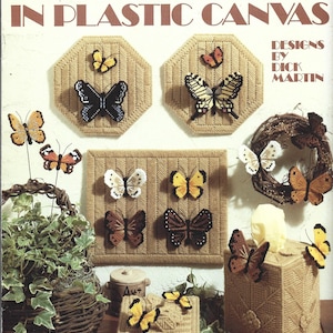 May include: A Leisure Arts craft leaflet 1102 titled Butterflies in Plastic Canvas with designs by Dick Martin. The cover displays various plastic canvas projects including wall hangings, a tissue box cover, and a small box, all featuring stitched butterfly motifs in yellow, black, white, and brown colors.