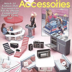 May include: A craft pattern book titled The Needlecraft Shop Fashion Doll Camper Accessories featuring instructions for 14 plastic canvas items including a picnic table, umbrella, lounge chairs, stove, microwave, and seating with pink and blue accents.