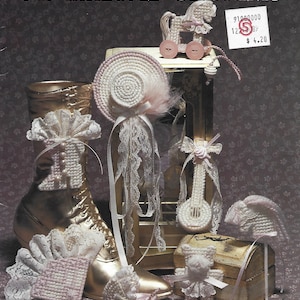 May include: A collection of plastic canvas ornaments including a rocking horse, hat, fan, carriage, teddy bear, and guitar. The items are crafted in white and pale pink with lace accents. The text reads PLASTIC CANVAS OLD FASHIONED ORNAMENTS SP-17.