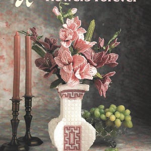 Peut inclure: Un livret de modèles d'artisanat en canevas plastique intitulé Annie's Attic Flowers Forever. La couverture présente un vase géométrique blanc et mauve rempli de fleurs crochetées roses et mauves, deux bougies brunes et des raisins verts.