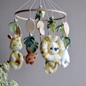 May include: A wooden baby mobile with felt animal toys. The mobile features a giraffe, lion, monkey, and a white animal with a long tail. The mobile is decorated with green felt leaves.