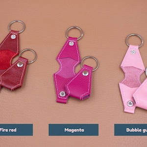 May include: Three pairs of leather keychains in fire red, magenta, and bubble gum pink. Each set includes one open and one closed keychain with a silver metal ring and snap button. Text labels below read Fire red, Magenta, and Bubble gum.