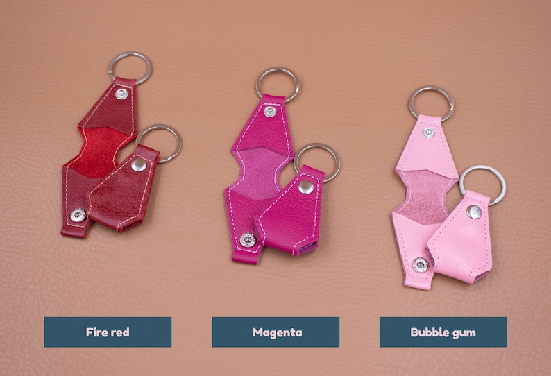 May include: Three pairs of leather keychains in fire red, magenta, and bubble gum pink. Each set includes one open and one closed keychain with a silver metal ring and snap button. Text labels below read Fire red, Magenta, and Bubble gum.