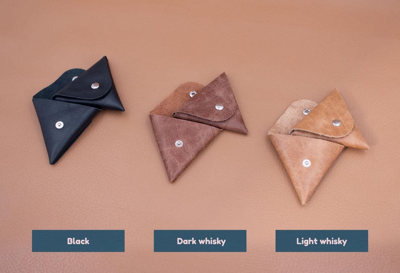 May include: Three leather coin purses in black, dark whisky, and light whisky colors. Each triangular pouch has a snap closure. The text below each purse reads "Black", "Dark whisky", and "Light whisky".