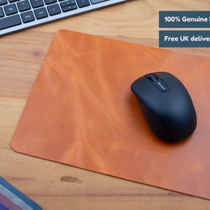 May include: A brown leather mouse mat with a black wireless mouse on top. The text "100% Genuine leather" and "Free UK delivery" is visible in the top right corner of the image.