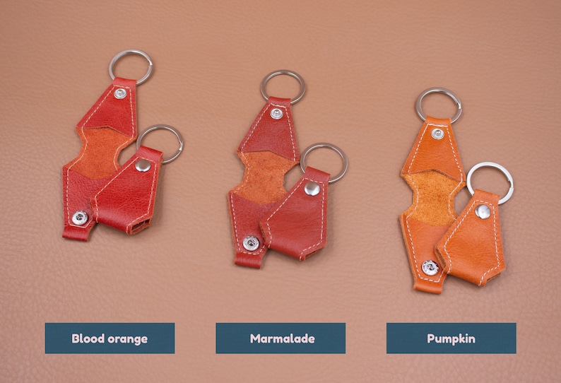 May include: Three leather keychains in blood orange, marmalade, and pumpkin colors. Each keychain features a metal ring and a snap-button closure. The text labels below each item read Blood orange, Marmalade, and Pumpkin respectively.
