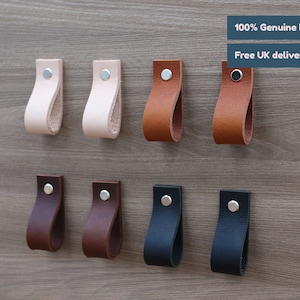May include: Eight leather cabinet pulls in various colours, including brown, black, and cream. The pulls are all the same shape, with a loop design and a silver screw. The text "100% Genuine leather" and "Free UK delivery" is visible at the top of the image.