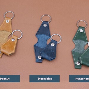 May include: Three sets of leather key covers with metal rings and snap buttons, displayed in peanut, storm blue, and hunter green colors. Each set includes a larger and a smaller cover, featuring visible stitching and silver-toned hardware components.