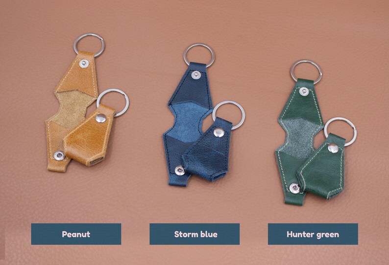 May include: Three sets of leather key covers with metal rings and snap buttons, displayed in peanut, storm blue, and hunter green colors. Each set includes a larger and a smaller cover, featuring visible stitching and silver-toned hardware components.
