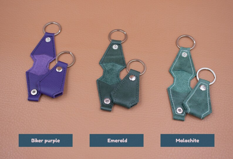 May include: Three sets of keychains in biker purple, emerald, and malachite colors. Each set includes a larger geometric-shaped leather piece with a metal ring and a smaller matching leather piece with a metal ring, both secured by silver snaps.