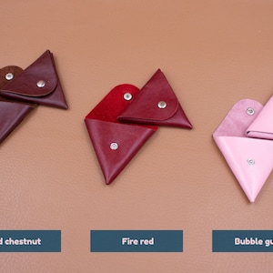 May include: Three leather coin purses in old chestnut, fire red, and bubble gum colors. Each triangular purse has a snap closure and is open to display the interior. The text below each purse reads "Old chestnut", "Fire red", and "Bubble gum".