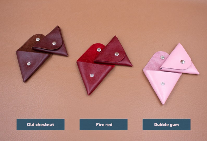 May include: Three leather coin purses in old chestnut, fire red, and bubble gum colors. Each triangular purse has a snap closure and is open to display the interior. The text below each purse reads "Old chestnut", "Fire red", and "Bubble gum".