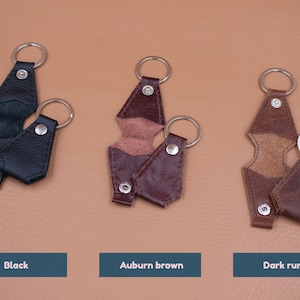 May include: Three leather key holders in black, auburn brown, and dark rum colors. Each holder features a metal split ring, a snap button closure, and a fold-over design. The text labels Black, Auburn brown, and Dark rum appear below each item.