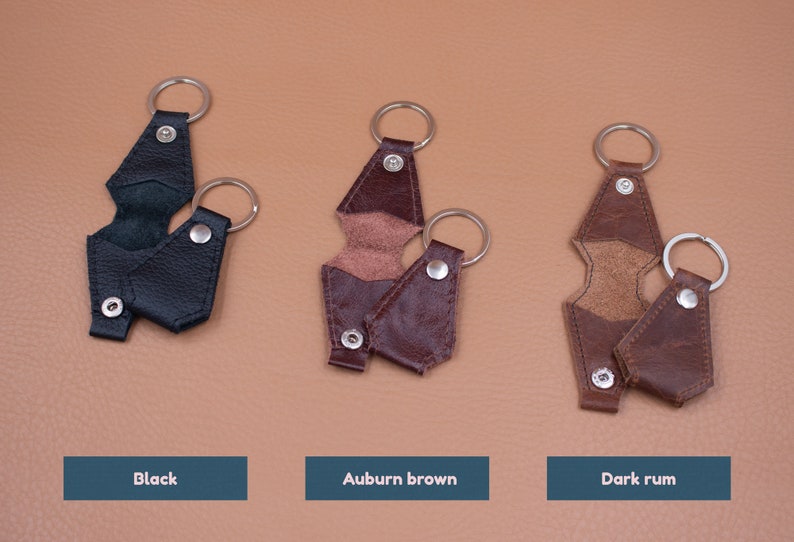 May include: Three leather key holders in black, auburn brown, and dark rum colors. Each holder features a metal split ring, a snap button closure, and a fold-over design. The text labels Black, Auburn brown, and Dark rum appear below each item.