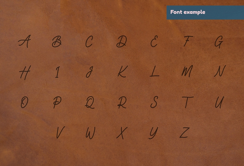 K&ouml;nnte beinhalten: Ein handgeschriebenes Alphabet in schwarzer Tinte auf braunem Lederhintergrund. Die Buchstaben sind in einem l&auml;ssigen, kursiven Stil geschrieben.