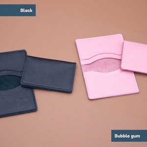 May include: Two leather card holders, one black and one pink. The black card holder has a suede interior. The pink card holder has a white interior. The text "Black" is above the black card holder and the text "Bubble gum" is below the pink card holder.