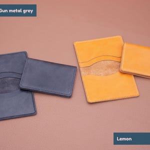 May include: Two leather wallets, one in gunmetal grey and one in lemon yellow. Both wallets have a similar design with two pockets and a suede lining.