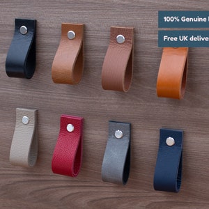 May include: Eight leather cabinet pulls in various colours, including black, brown, beige, red, grey, and blue. Each pull has a silver metal screw in the centre.